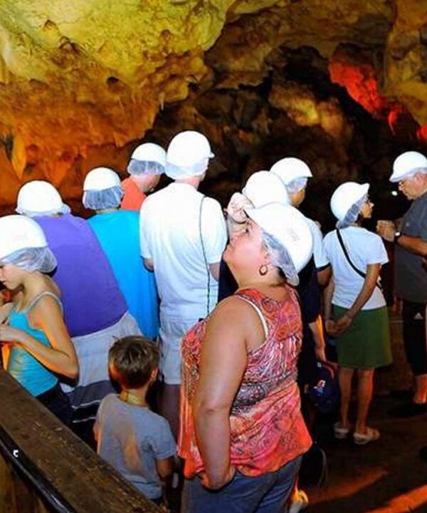 In the very last spot of the Green Grotto Caves in St. Ann, Jamaica, 15 visitors, some who came in a ride with Island Turf Tours, stop to look over into the watery area. In the foreground a woman dressed in a light pink blouse looks up at the cave formations while others listen to the tour guide. The lights are turned on because this section is normally very dark.