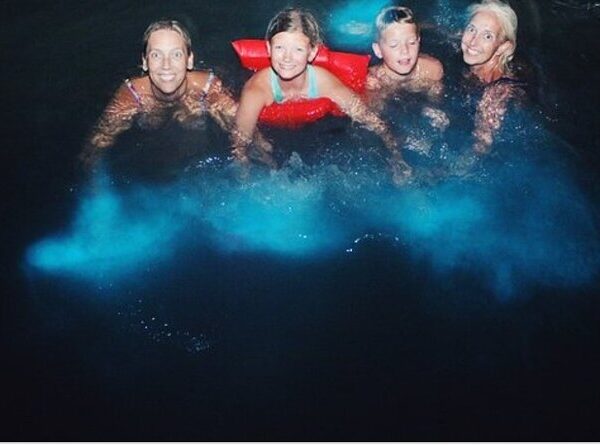 Four of Norris’ hotel transfer guests to the Luminous Lagoon swim attraction were carried here to Falmouth, Trelawny, on Jamaica’s north coast and they are enjoying themselves in the water. The close-up shot sees two adult ladies flanking the two kids, a girl and boy, in between, and the girl has the red floats around her bust. The dark water glows light blue as they’re wading their hands inside the ocean.