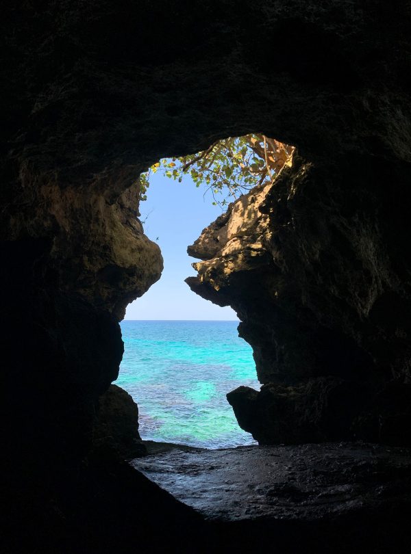 A view of the Caribbean Sea from the caves of the Xtabi on the Cliffs Resort in Negril – a popular hotel, swim and snorkel spot for Norris’ guests who travel to Jamaica. Inside is dark and in this part of the cave forms an hourglass shape as you peer out to see the sea beyond. A few tree branches and leaves hang from the top opening.