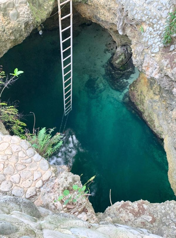 Looking down into the Blue Hole Mineral Spring in Negril. The inner rocky cave has water below and a ladder that stretches down into it, a frequent travel spot for tourists visiting Jamaica.