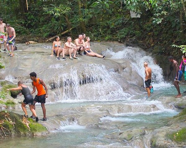 Several guests liaise around the Mayfield Falls and a couple of guides can be seen helping guests to climb onto the rocks in this serene scene.