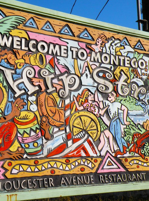 The main 2+ meter sign of a colorful wooden-created mural relief welcomes guests to the city by saying “Welcome to Montego Bay’s Hip Strip”, put up by the Gloucester Avenue Restaurant Association. It shows a Rastafarian playing the drum on the left, a flute-player at the upper left some drinks in the foreground, a couple dancing and having a great time, and food and shops on the right.
