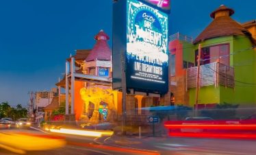 The colorful streets of Montego Bay light up in the evening as cars whizz by in the popular city for Norris’ guests. A Large Media screen sign showing “Coral Cliff Got Talent” is prominently seen showing an advert for the local talent auditions, and a small Burger King sign sits calmly beneath it. Palm trees can be seen off in the distance on the opposite left.