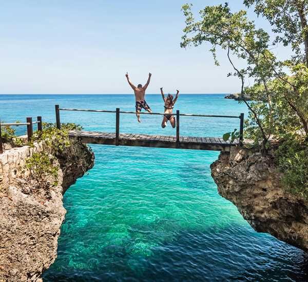 A couple that Norris carried are captured airborne from behind, as they lunge from a bridge platform into the waters below, at Rockhouse, Negril.