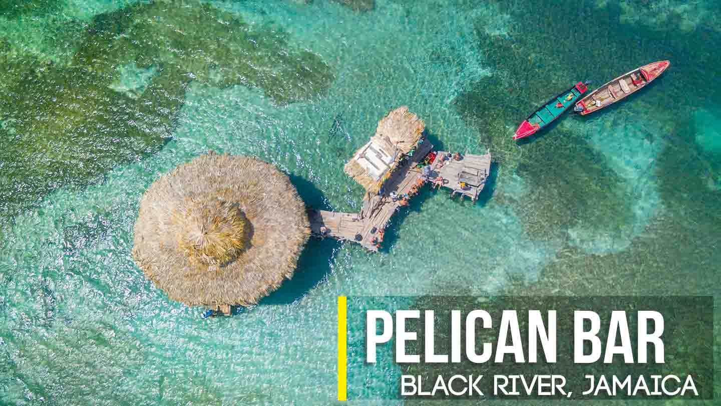 An overhead shot of the Pelican Bar, off the coast of Black River, St. Elizabeth where Norris frequently carries travelers visiting Jamaica in his Montego Bay to Negril private airport transfer tour service. Here, tourists can be seen sitting on the walkway platform hanging out and talking as the green waters and two small fishing-like boats surround the calm sunny scene.